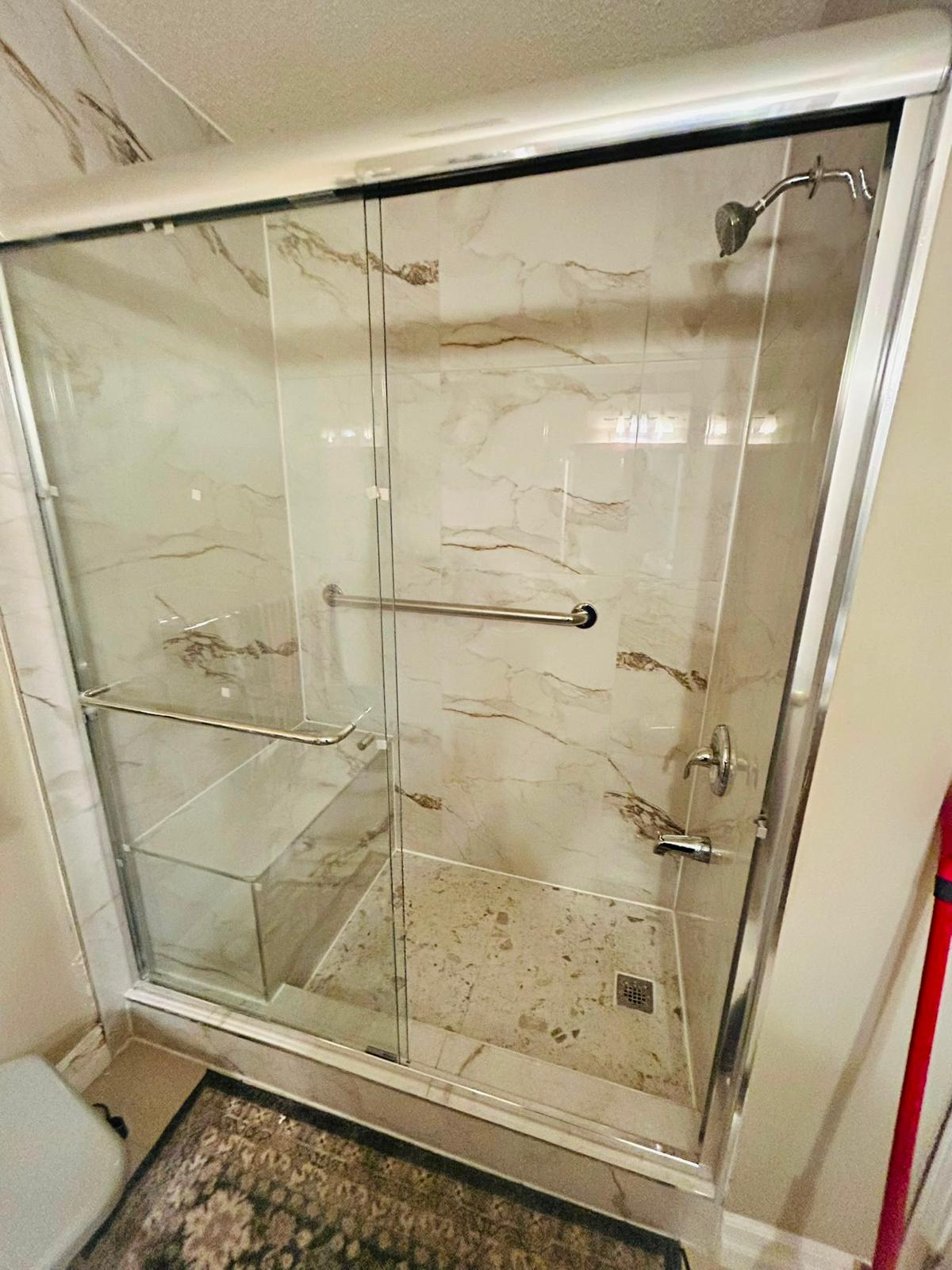 After — walk-in shower with marble tile and glass doors